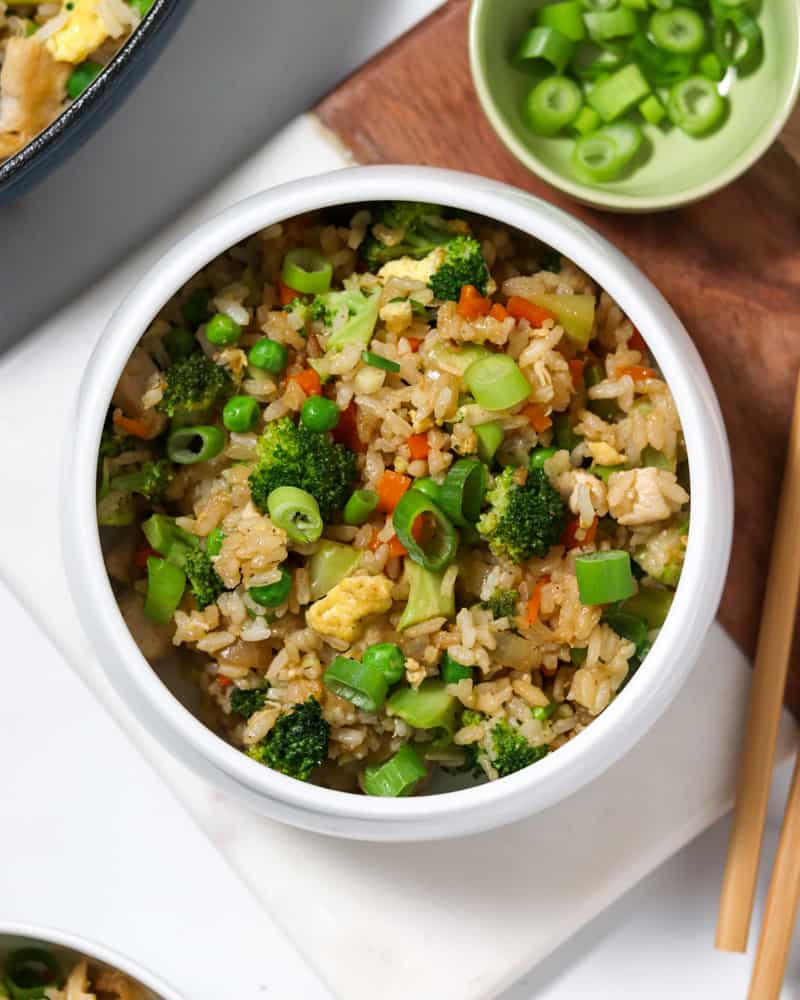 A colorful bowl of chicken fried rice with broccoli, carrots, peas and green onions