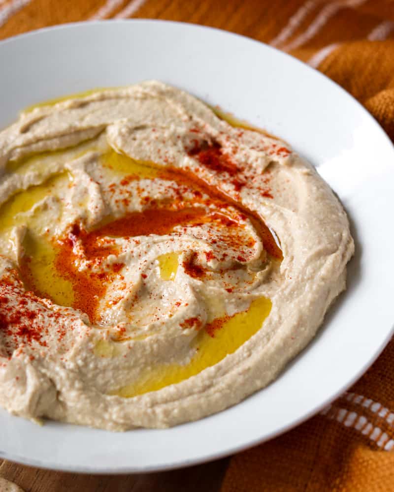 A close-up shot of a bowl of creamy hummus, showcasing the swirls of olive oil and smoked paprika