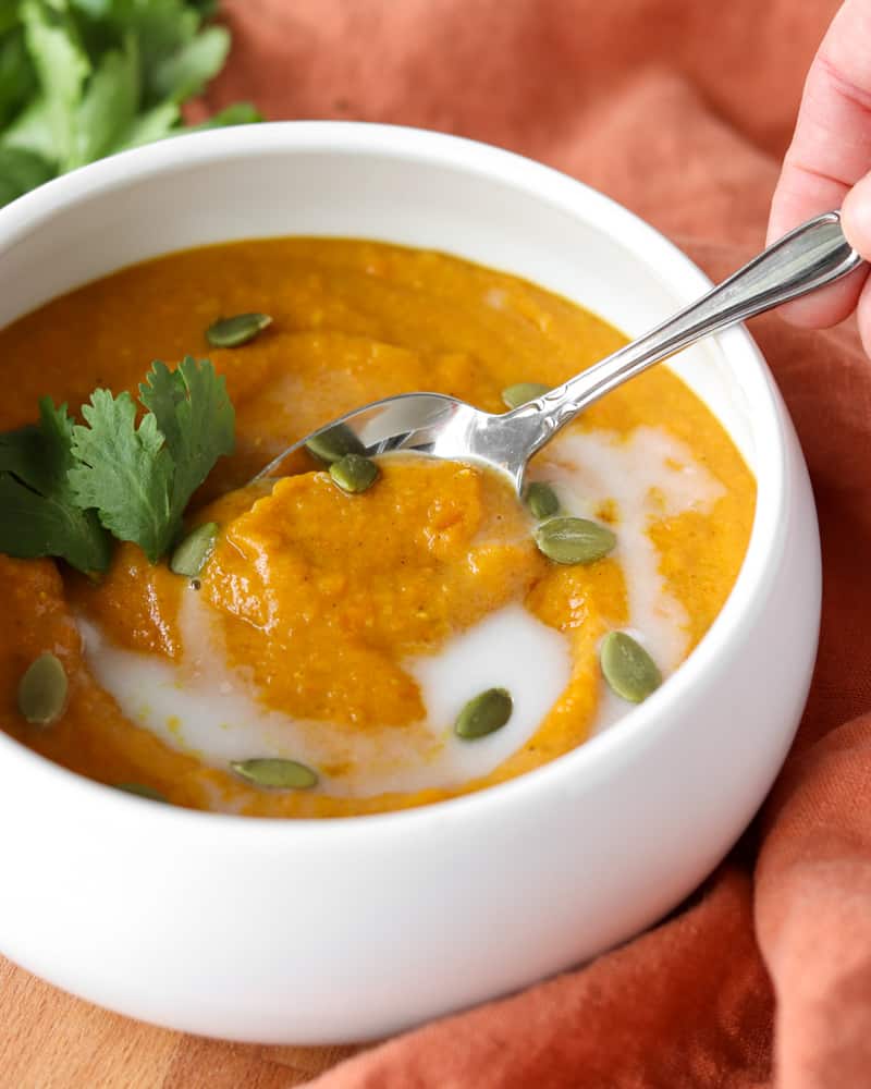 A bowl of thick curried carrot and sweet potato soup, swirled with coconut milk and topped with pumpkin seeds