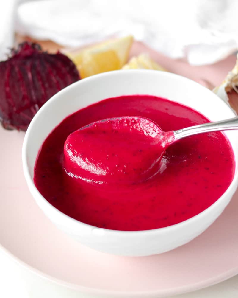 A spoon in a small bowl of bright pink Greek dressing