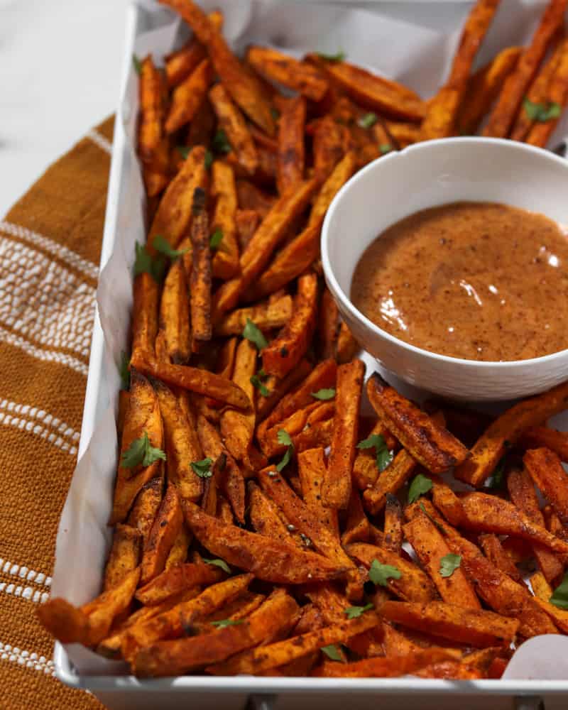 A serving tray full of crispy spiced sweet potato fries with a ramekin of honey-chipotle mayo