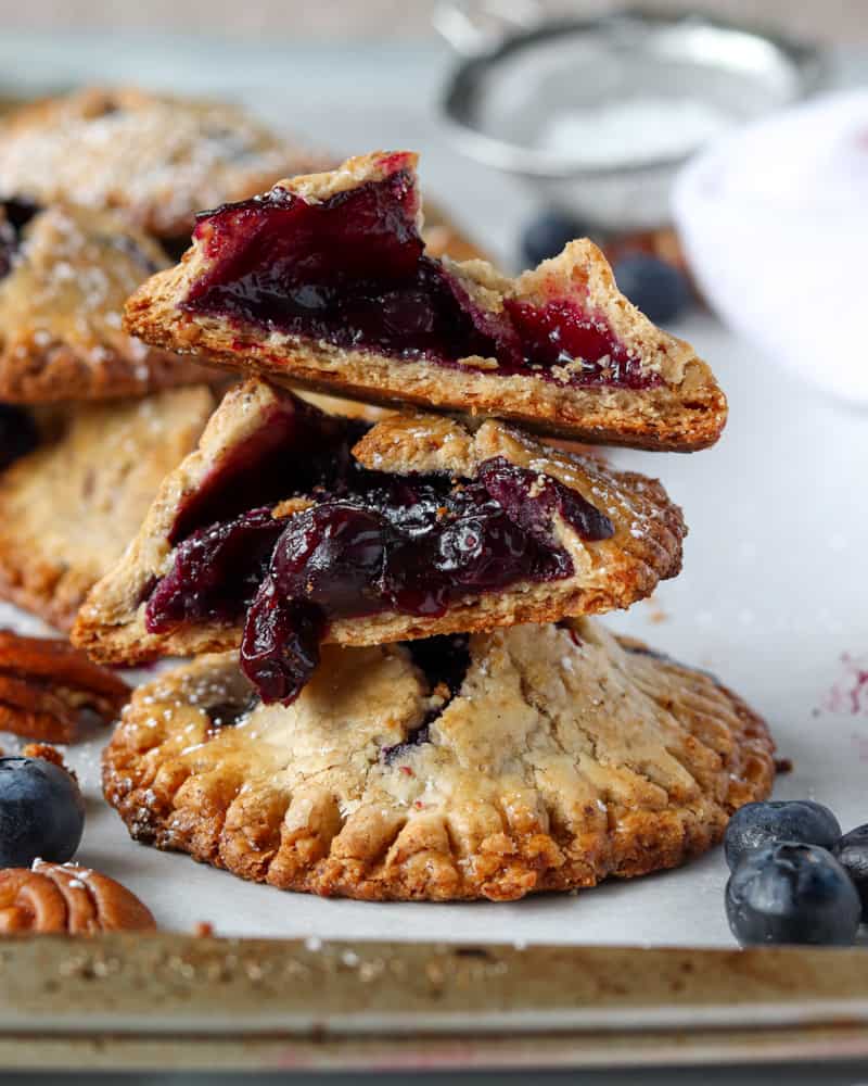 A stack of blueberry pecan hand pies, torn down the middle to show the juicy blueberry filling inside