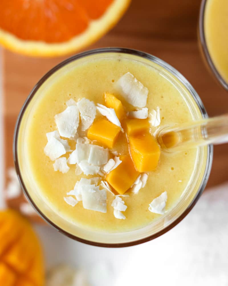 Fresh mango cubes and coconut flakes on top of a glass of tropical mango pineapple smoothie