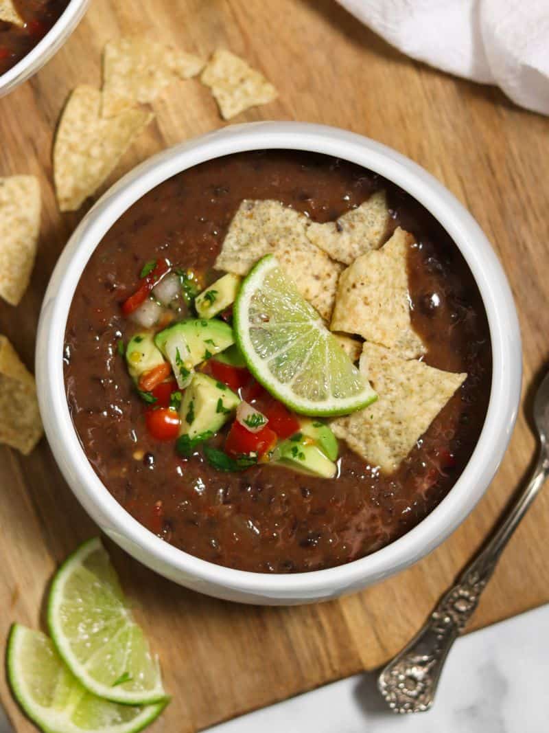 A bowl of black bean soup topped with avocado salsa, tortilla chips and a lime wedge