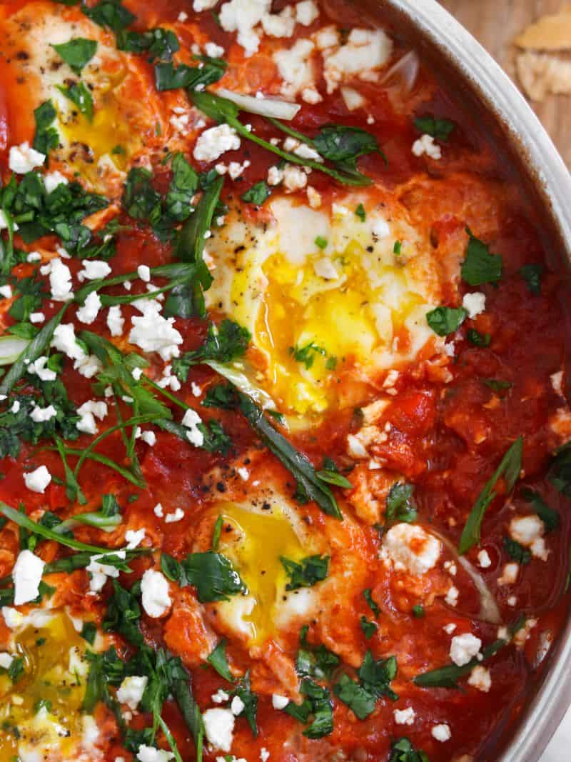 Runny, golden egg yolks in a pan of spicy tomato sauce, topped with lots of feta, parsley and green onion