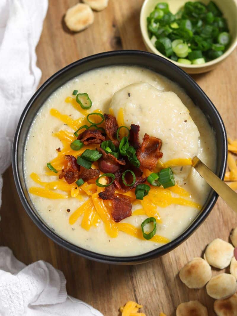 A bowl of creamy potato soup topped with bacon, cheddar cheese and green onions