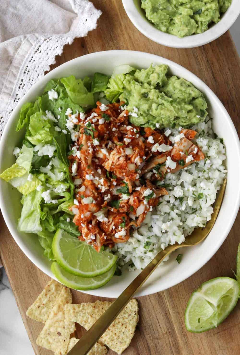 A big bowl with cilantro-lime rice, chicken tinga, guacamole, lettuce and lime wedges