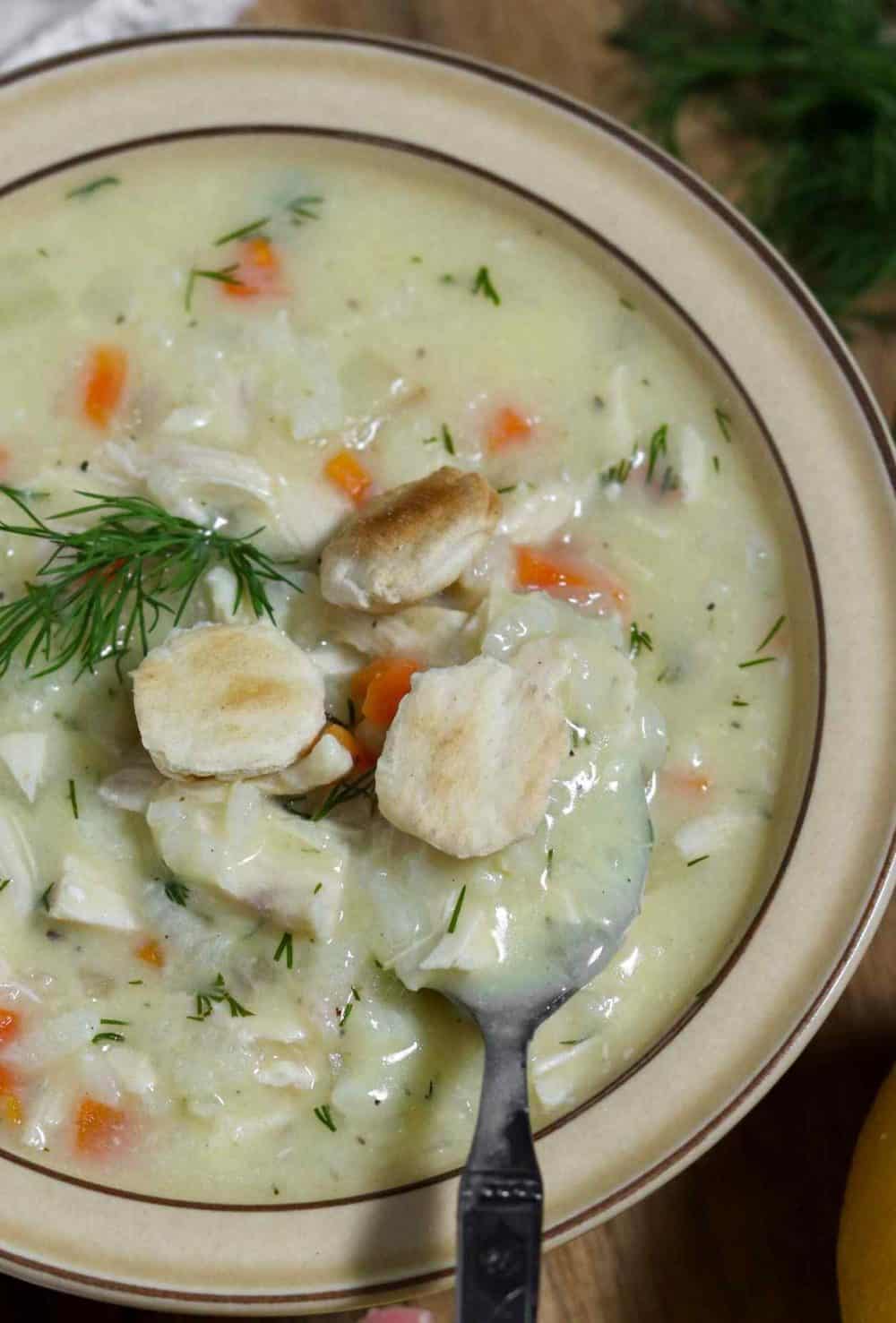 A bowl of lemon rice soup topped with oyster crackers, with a spoon in it