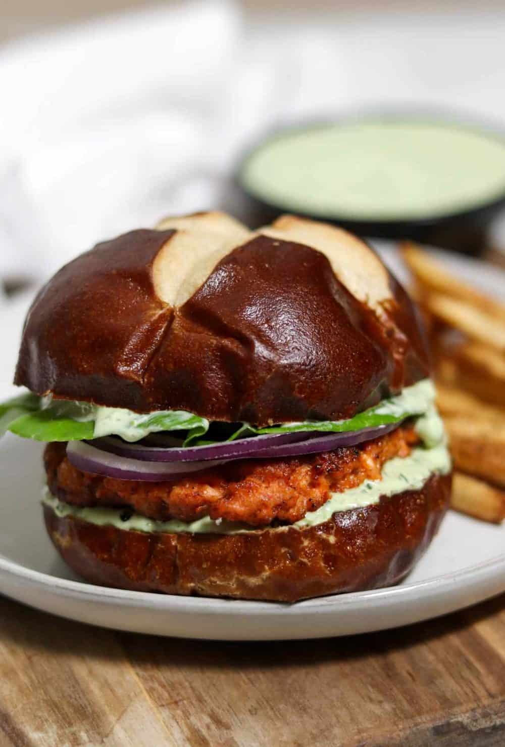 A blackened salmon burger on a pretzel bun with lots of creamy lemon herb sauce, lettuce and red onion. And fries on the side, of course!