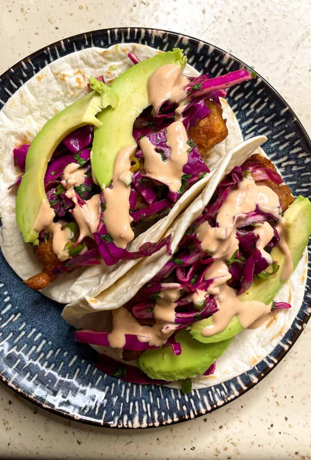 Two tacos filled with crispy beer battered fish, tangy red cabbage slaw, sliced avocado, and smoky chipotle crema