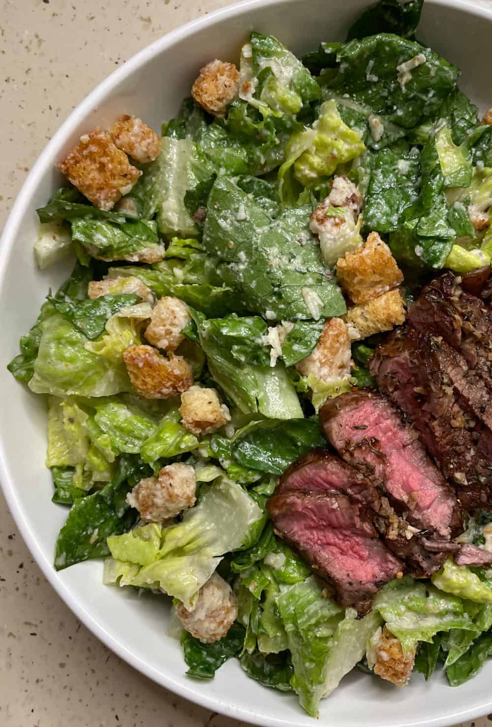 Caesar salad topped with crisp, golden-brown croutons and juicy medium-rare steak