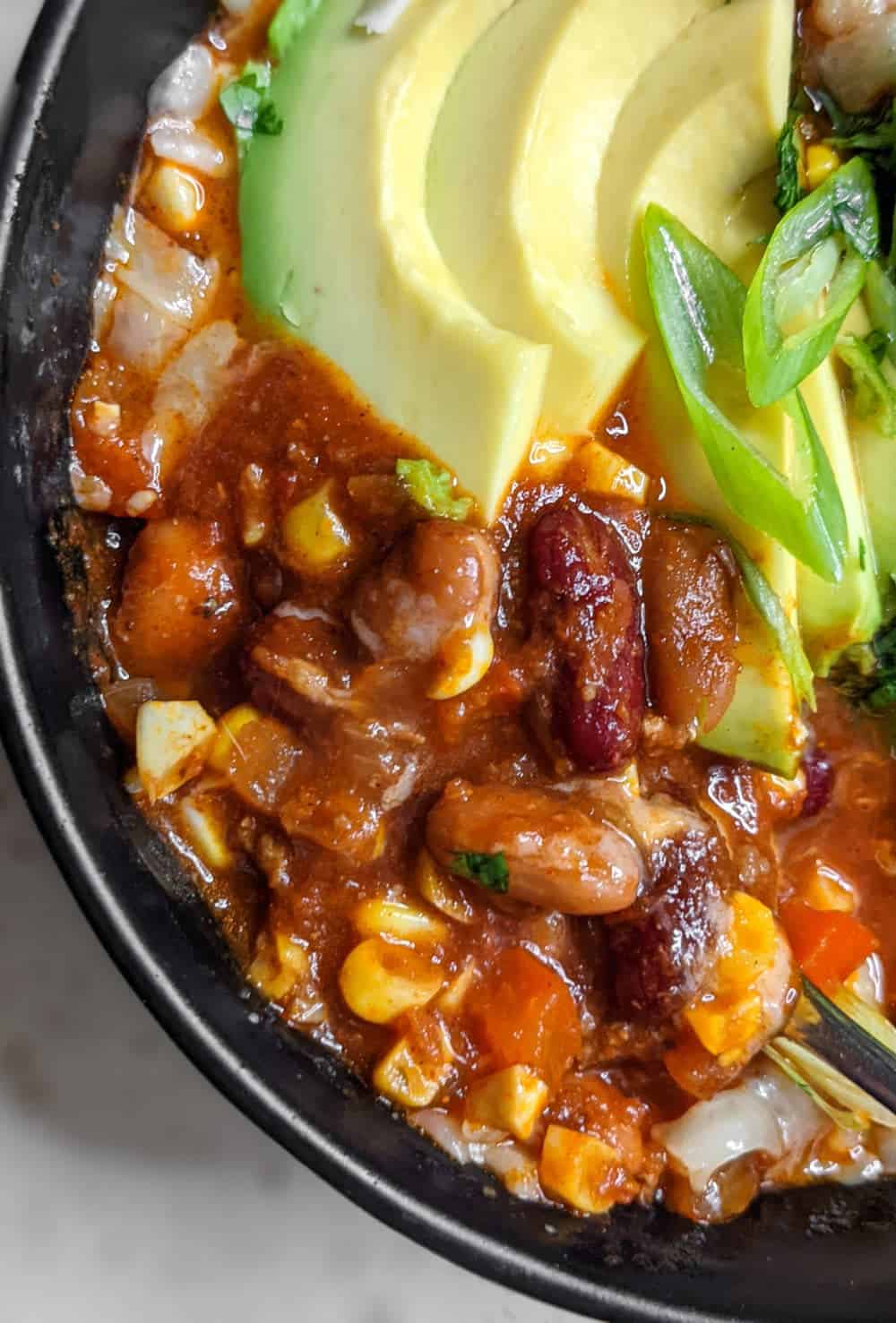 A bowl of beef and bean chili topped with avocado slices, green onions, and cilantro