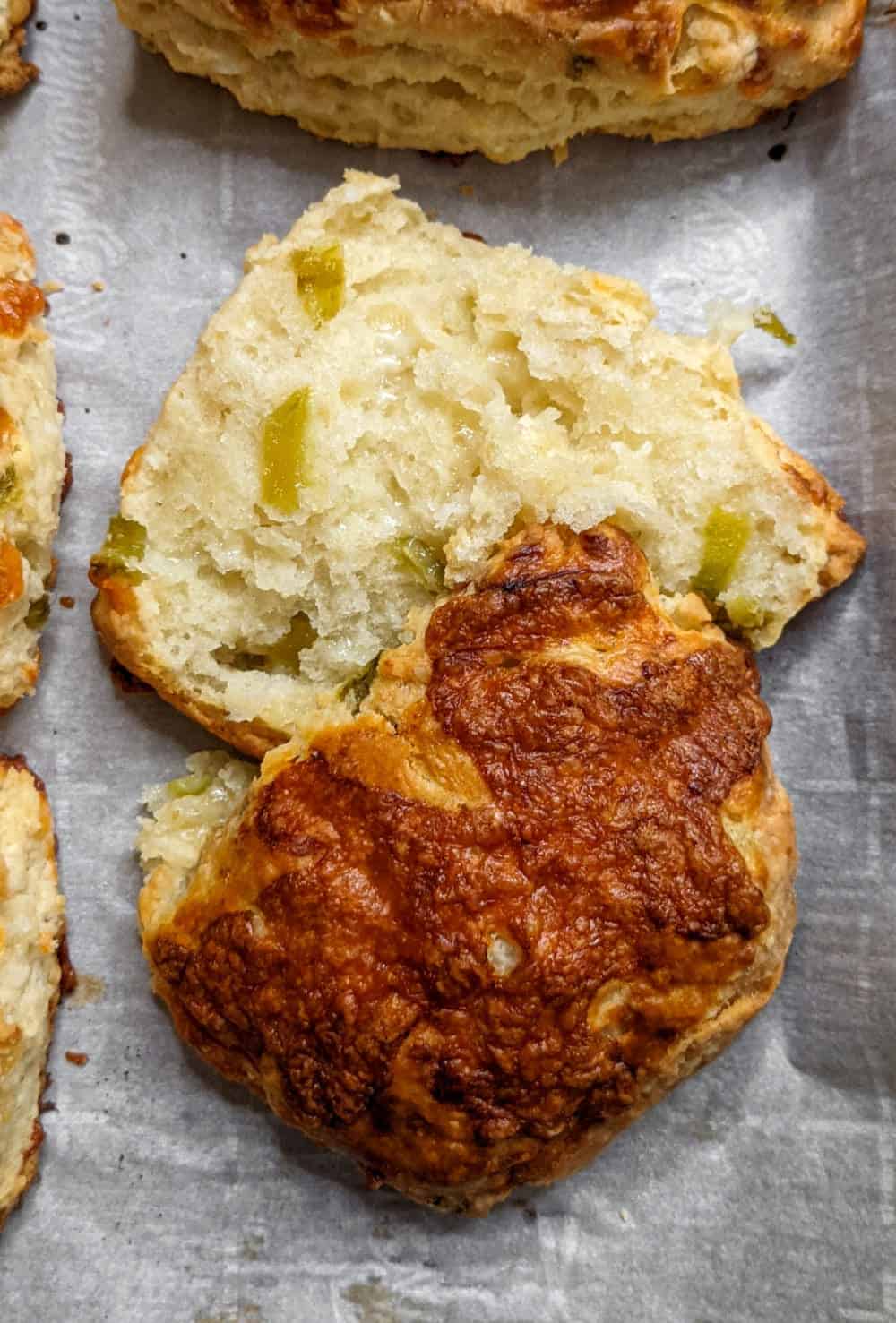 A fresh biscuit split in half, with crispy melted cheese on top and roasted green chiles in the middle