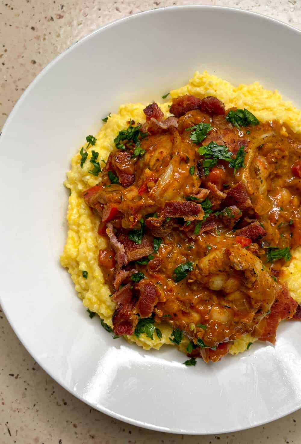 A bowl of creamy cheddar grits topped with cajun-spiced shrimp, crumbled bacon and parsley