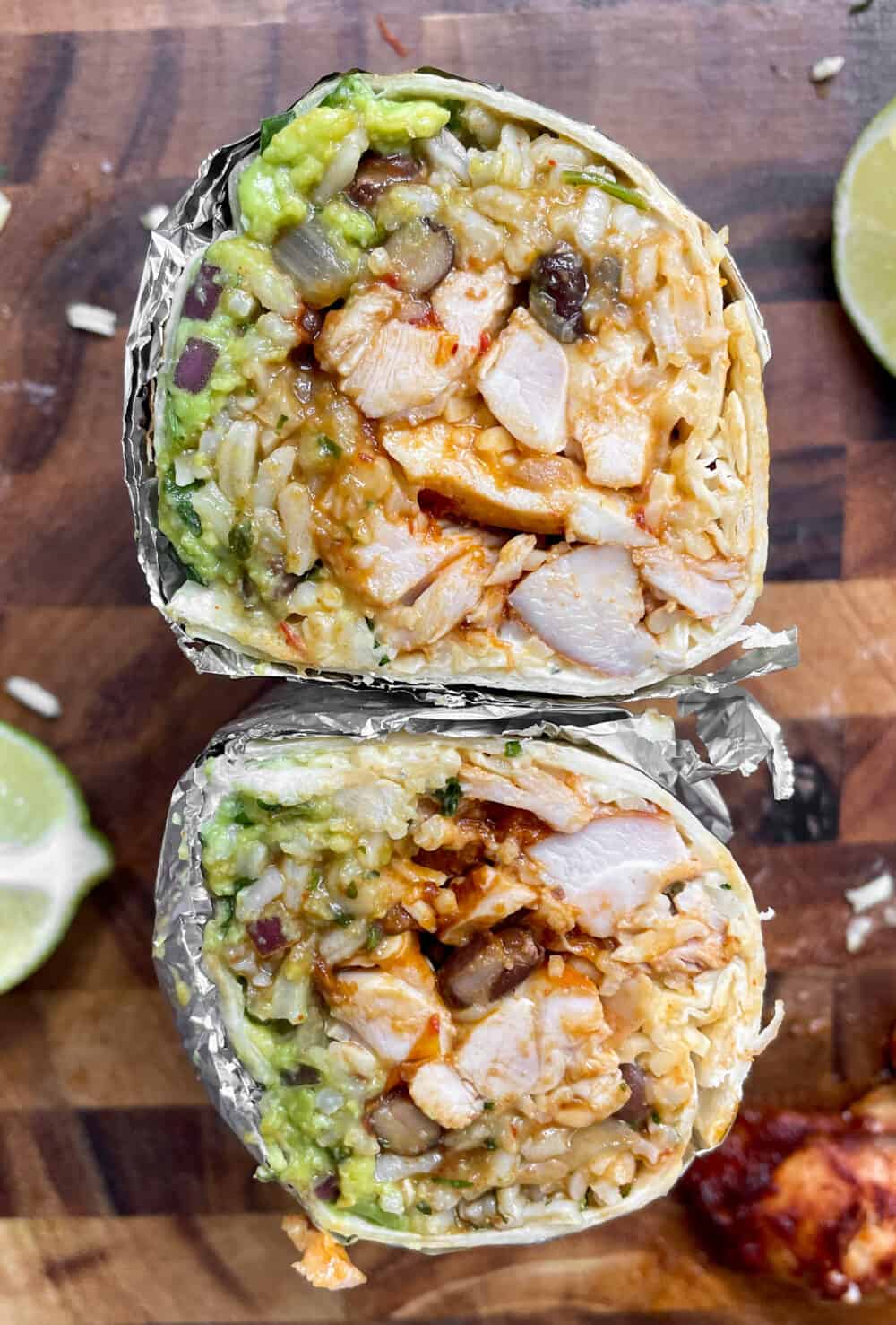 A burrito, wrapped in foil and sliced in half to show what's inside: cilantro lime rice, black beans, chipotle chicken, guacamole, cheese and sour cream.