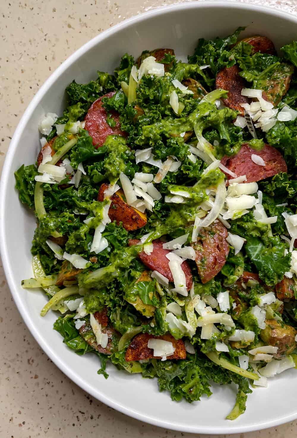 A bowl heaping with vibrant kale, crisp potatoes, chorizo, shredded cheese, and bright green mojo verde vinaigrette.