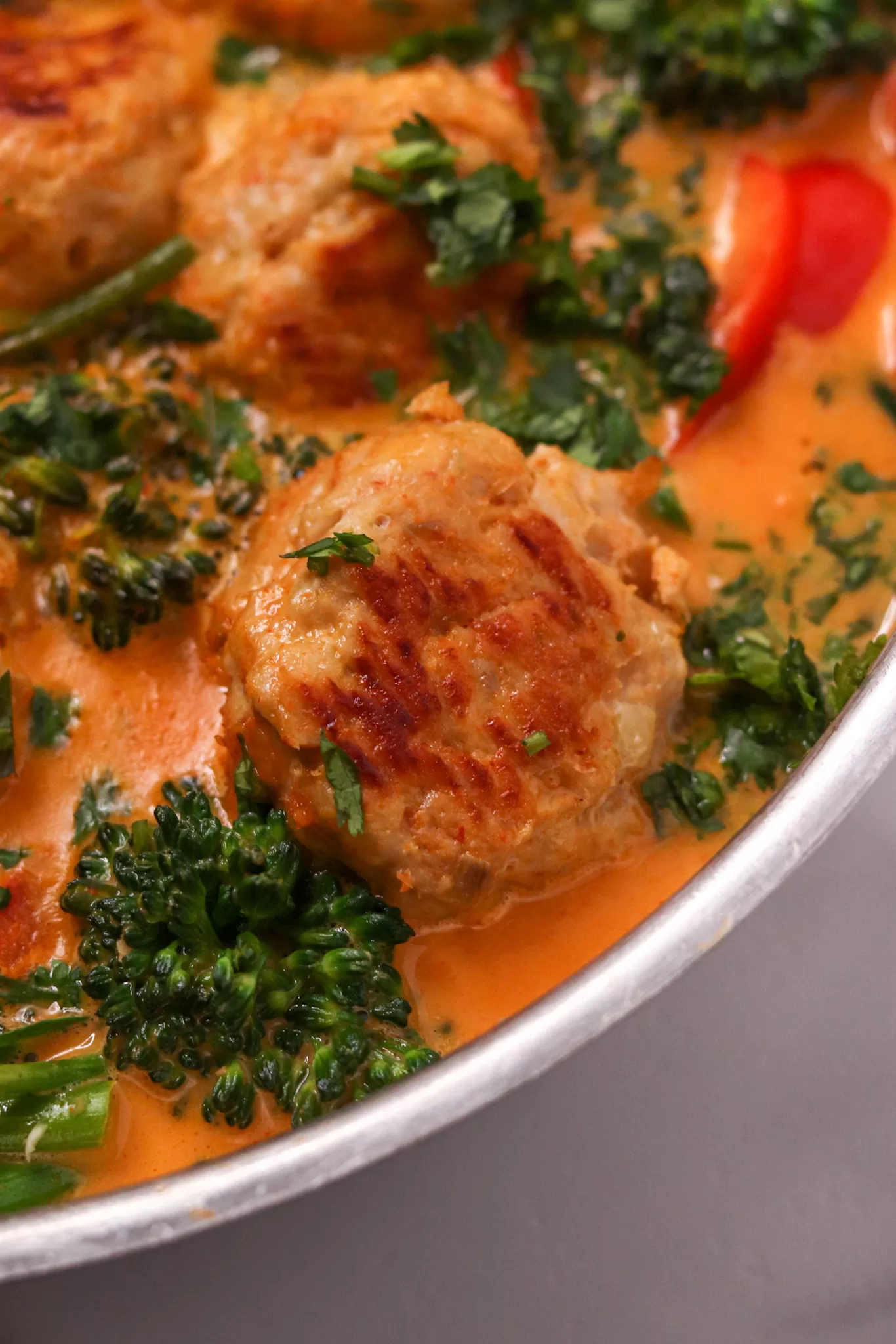 A close-up of a perfectly browned chicken meatball afloat in a pan of coconut curry sauce and veggies.