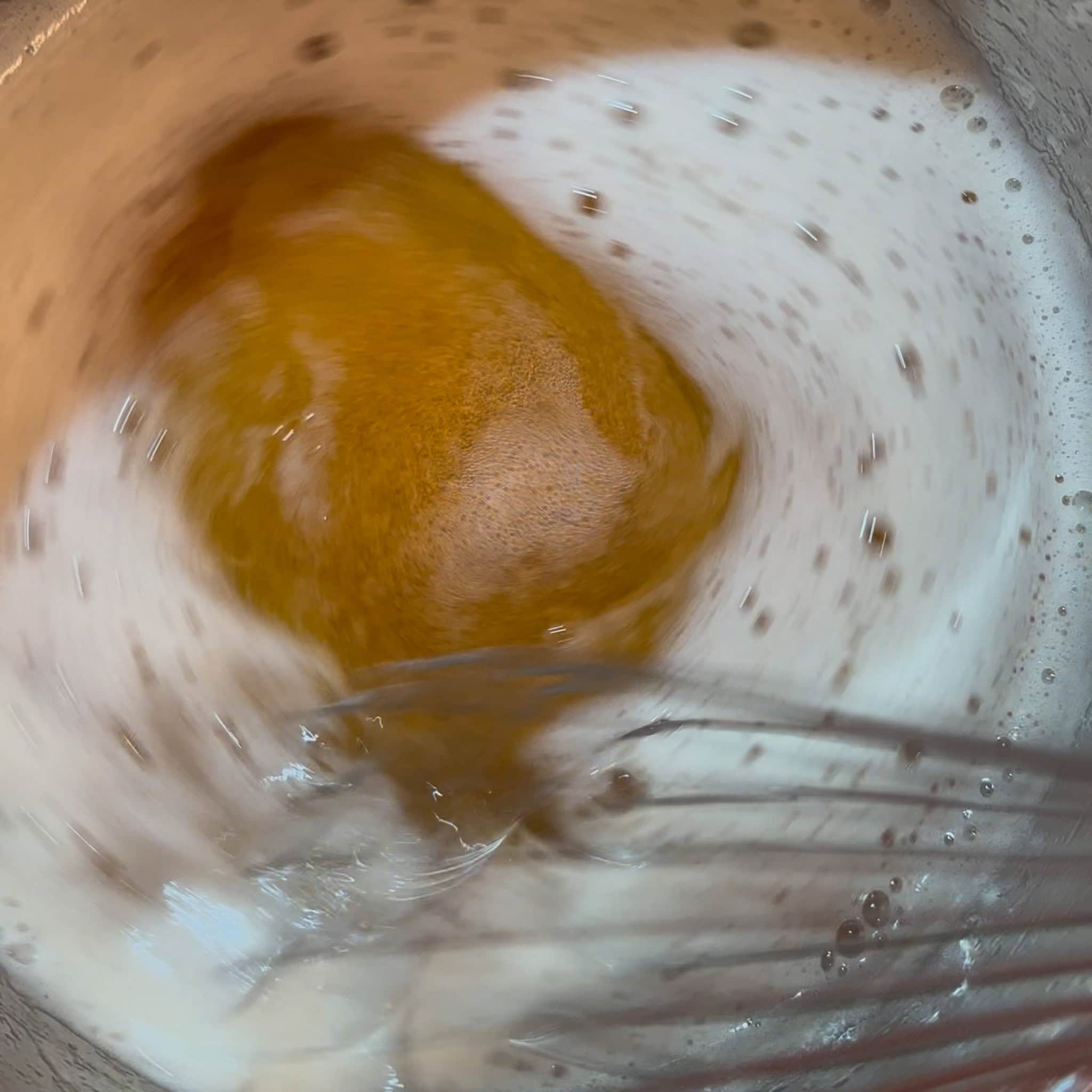 Amber-colored brown butter being whisked in a saucepan.